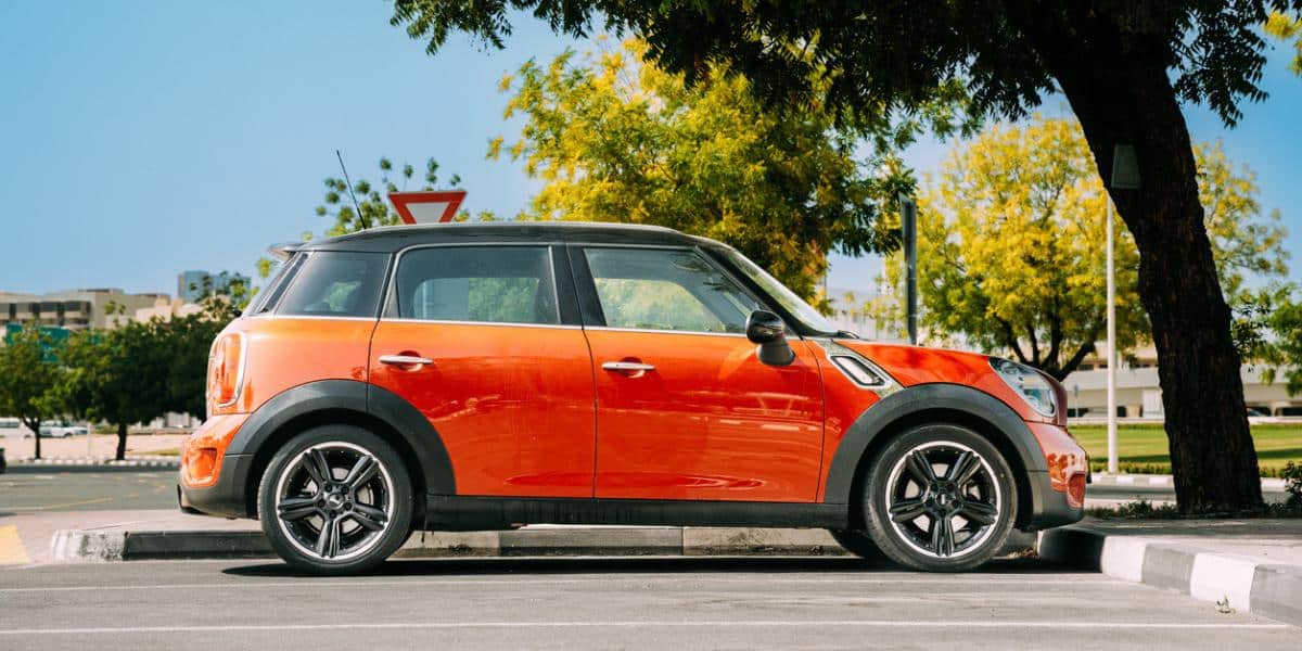 A side view of an orange Mini Cooper Countryman parked in a parking spot.