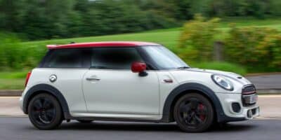 A white 2024 Mini JCW driving on a highway in front of a green landscape.