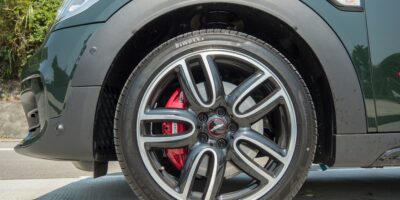 Close-up view of the front wheel of a 2025 Mini JCW featuring stylish alloy rims, Pirelli tires, and red brake calipers on a sunny day