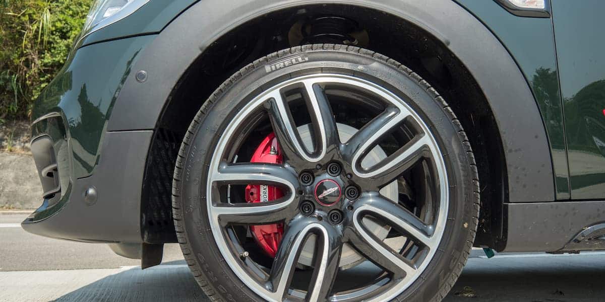 Close-up view of the front wheel of a 2025 Mini JCW featuring stylish alloy rims, Pirelli tires, and red brake calipers on a sunny day