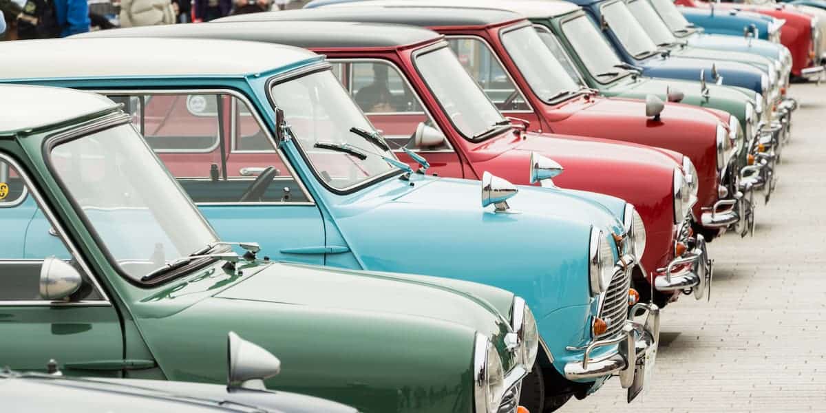 A lineup of classic Mini Coopers in various colors at an outdoor event. The history of Mini Cooper generations showcases its timeless design and charm.