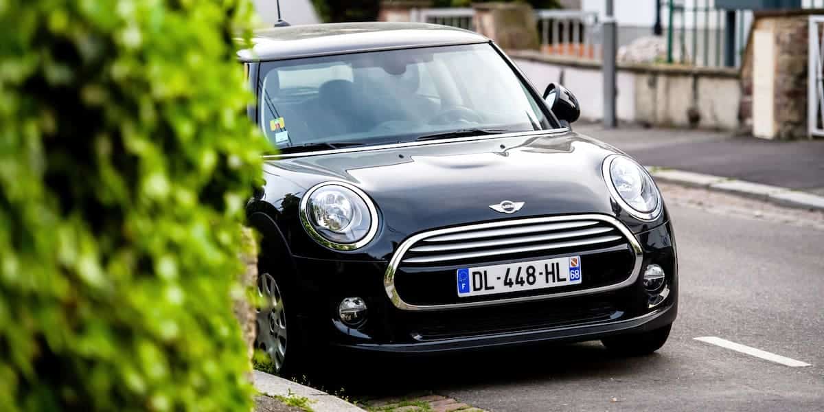 A black modern Mini Cooper parked on a residential street. The evolution of Mini Cooper generations has transformed this classic into a modern icon.