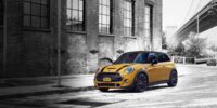Yellow MINI Cooper S with racing stripes parked on city street - the iconic brand many wonder who owns MINI Cooper since BMW's acquisition in 2000