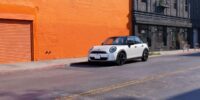 White MINI Cooper parked on urban street requiring collision repair after accident damage with orange building backdrop