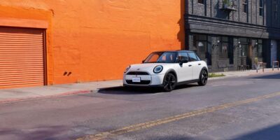 White MINI Cooper parked on urban street requiring collision repair after accident damage with orange building backdrop