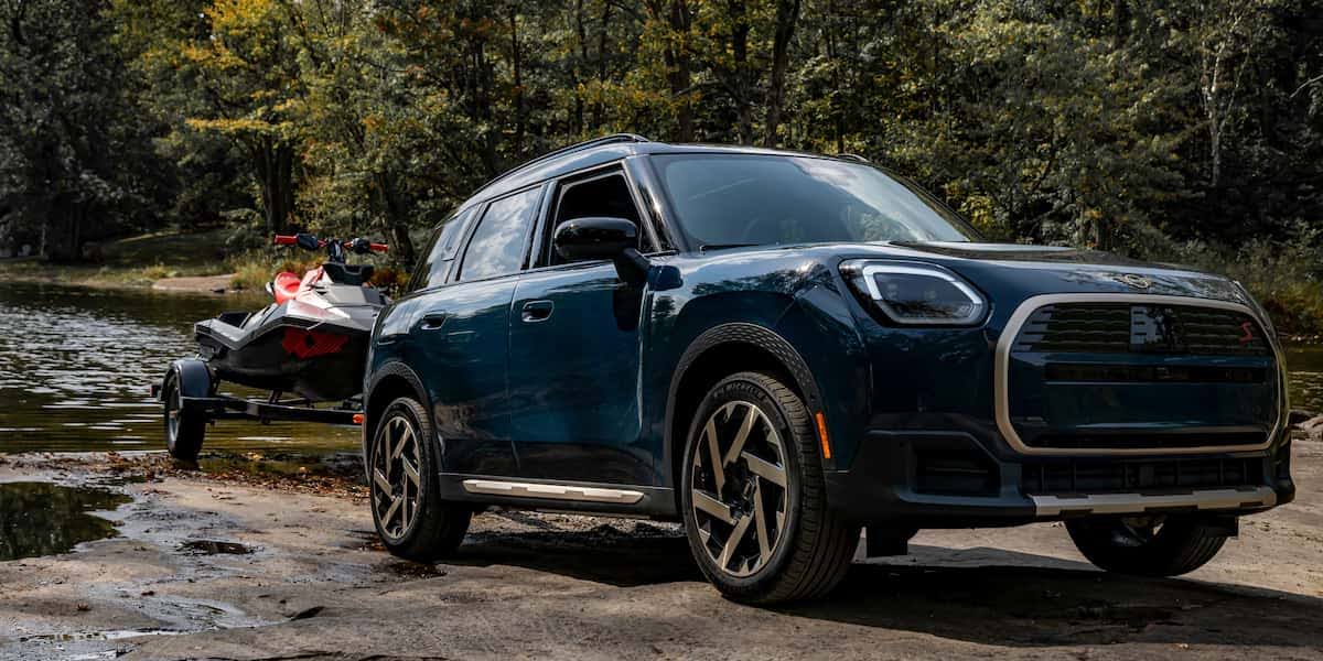 Mini Cooper SUV towing a jet ski near a lake, parked on rocky ground, showcasing mini cooper tires in an outdoor all-terrain setting.