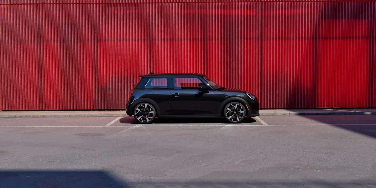 Black Mini Cooper parked in front of a red wall at a mini dealership showcasing style and personality.