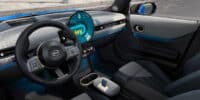 Interior of a MINI car showing dashboard and OLED screen running Mini operating system 9 with modern controls and voice assistant display.