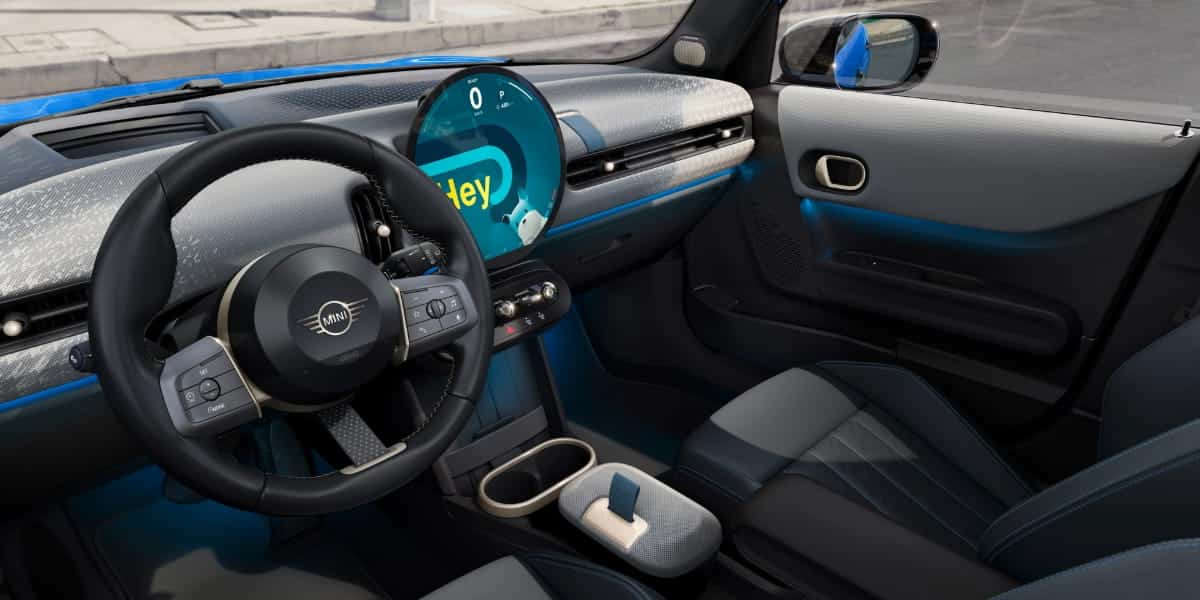 Interior of a MINI car showing dashboard and OLED screen running Mini operating system 9 with modern controls and voice assistant display.